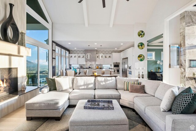 living room with ceiling fan, light wood-type flooring, beamed ceiling, and a high ceiling