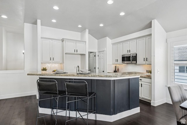 6228 W Apollo Way, Highland, UT 84003 - kitchen with a kitchen bar, an island with sink, tasteful backsplash, dark wood-type flooring, and light stone countertops