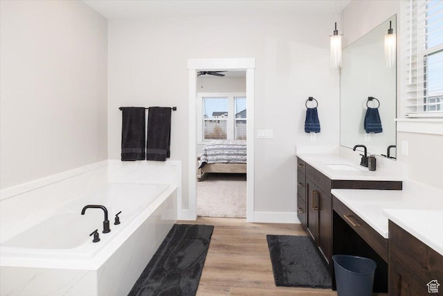 bathroom featuring ceiling fan, wood-type flooring, tiled tub, and vanity