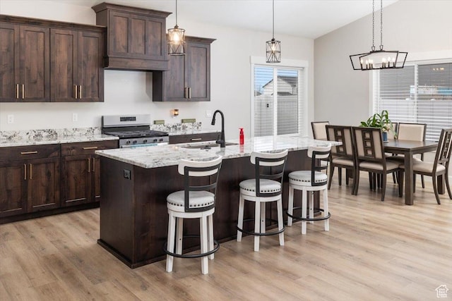 kitchen featuring stainless steel gas stove, sink, pendant lighting, and an island with sink