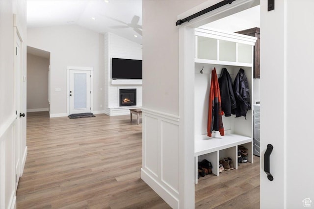mudroom featuring a brick fireplace, lofted ceiling, ceiling fan, and light wood-type flooring