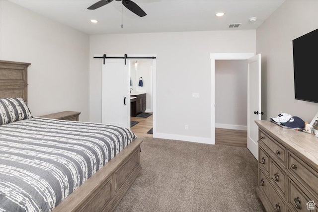 carpeted bedroom featuring ensuite bathroom, a barn door, and ceiling fan