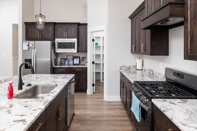 kitchen featuring dark brown cabinetry, stainless steel appliances, sink, hanging light fixtures, and premium range hood