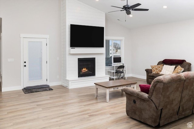living room featuring ceiling fan, a large fireplace, light hardwood / wood-style floors, and high vaulted ceiling