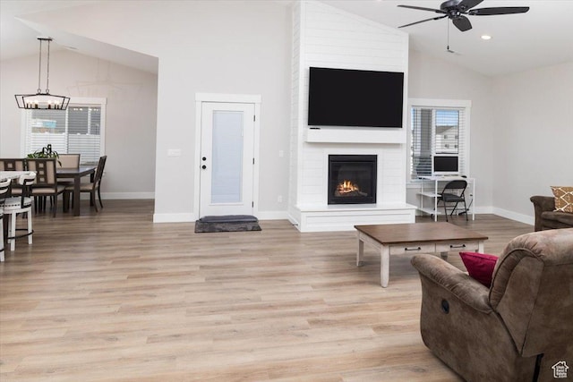 living room with lofted ceiling, ceiling fan, a large fireplace, and light hardwood / wood-style floors