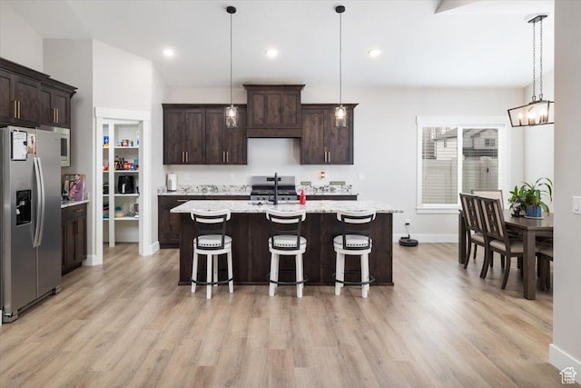kitchen with pendant lighting, appliances with stainless steel finishes, dark brown cabinetry, a center island with sink, and a breakfast bar area