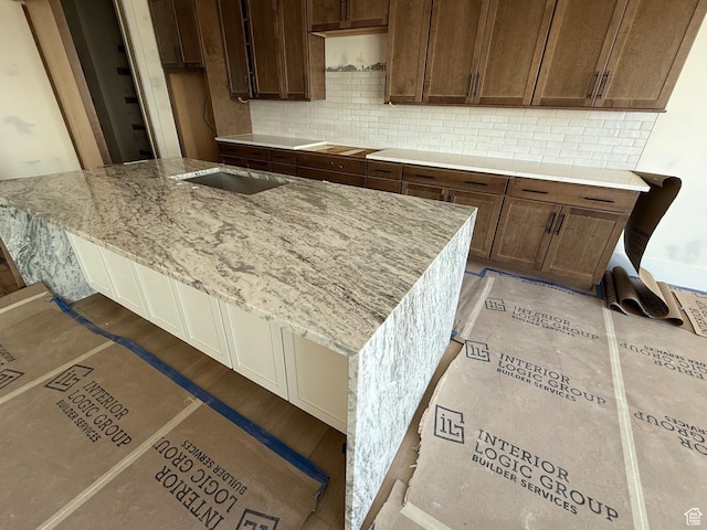 kitchen featuring a kitchen island with sink, light tile patterned floors, tasteful backsplash, and light stone countertops
