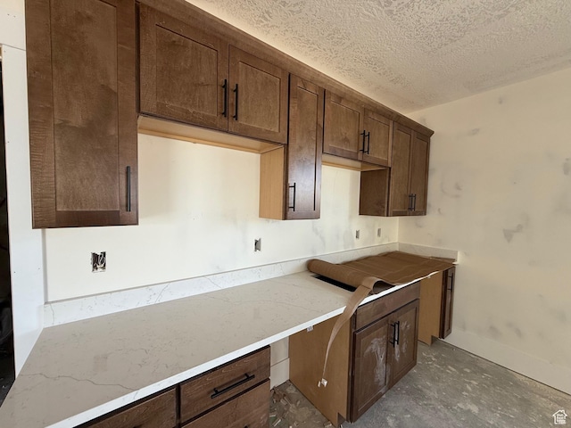 kitchen featuring baseboards, dark brown cabinetry, a textured ceiling, and built in desk