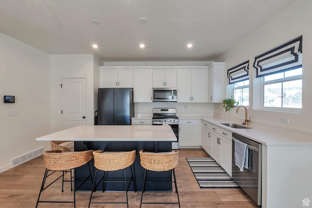 kitchen with white cabinetry, light hardwood / wood-style floors, stainless steel appliances, sink, and a center island