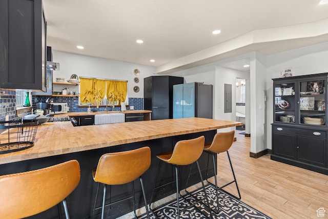 87 N 100 W, Marysvale, UT 84750 - kitchen featuring light hardwood / wood-style floors, kitchen peninsula, butcher block countertops, backsplash, and a breakfast bar