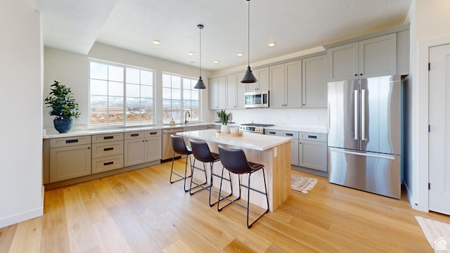 kitchen with appliances with stainless steel finishes, pendant lighting, light hardwood / wood-style flooring, a breakfast bar, and a center island