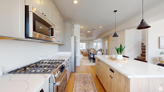 kitchen featuring decorative light fixtures, a kitchen island, white cabinetry, light stone countertops, and appliances with stainless steel finishes