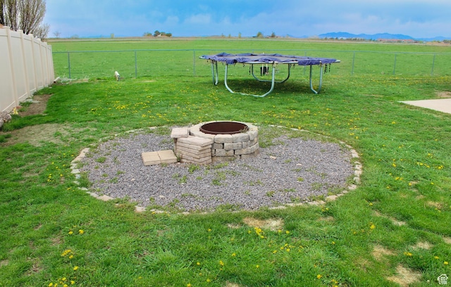 view of yard featuring fence, a trampoline, an outdoor fire pit, and a rural view