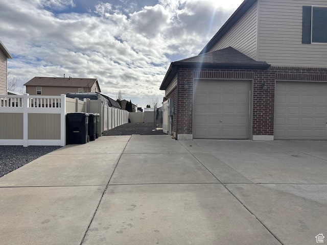 view of side of home featuring fence, driveway, and brick siding