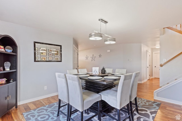 dining area with light wood-type flooring, baseboards, and stairway