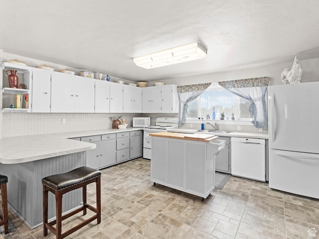 kitchen with white appliances, sink, backsplash, white cabinets, and a breakfast bar area