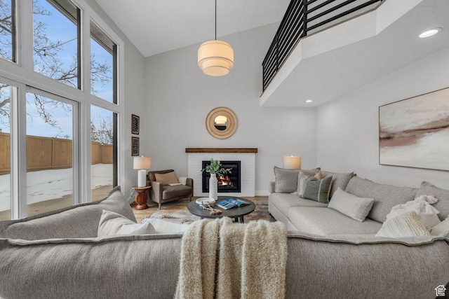 living area featuring wood finished floors, plenty of natural light, a high ceiling, and a brick fireplace