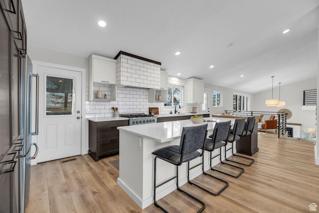 kitchen with light wood-style flooring, tasteful backsplash, light countertops, custom range hood, and a breakfast bar area