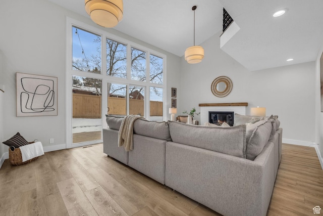 living area with light wood-style flooring, high vaulted ceiling, baseboards, and a brick fireplace
