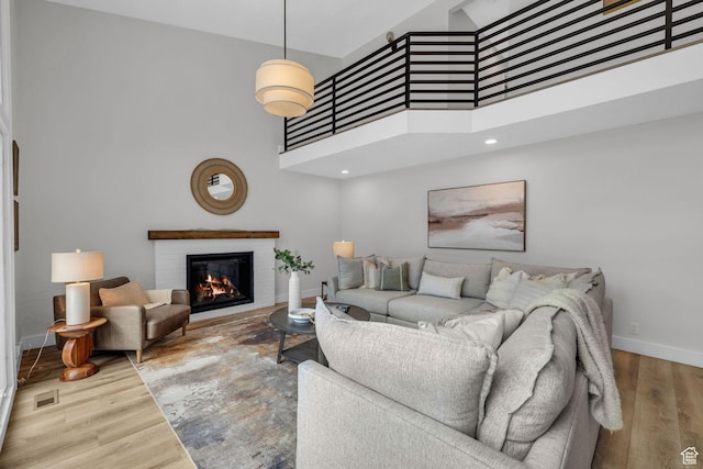 living room featuring visible vents, a high ceiling, wood finished floors, a brick fireplace, and baseboards