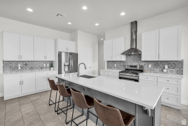 kitchen with a kitchen bar, sink, a kitchen island with sink, stainless steel appliances, and wall chimney exhaust hood