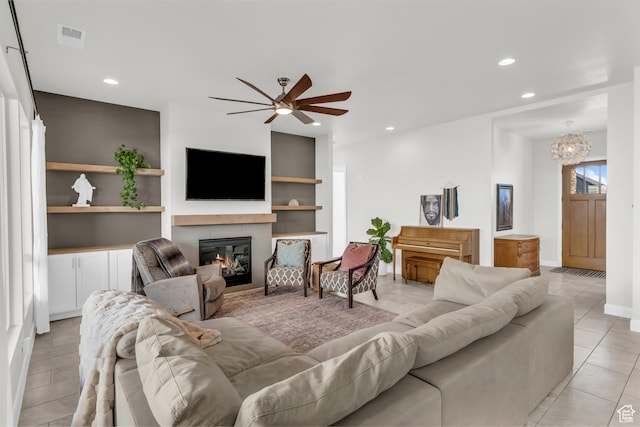 living room with ceiling fan with notable chandelier, light tile patterned floors, built in features, and a tiled fireplace