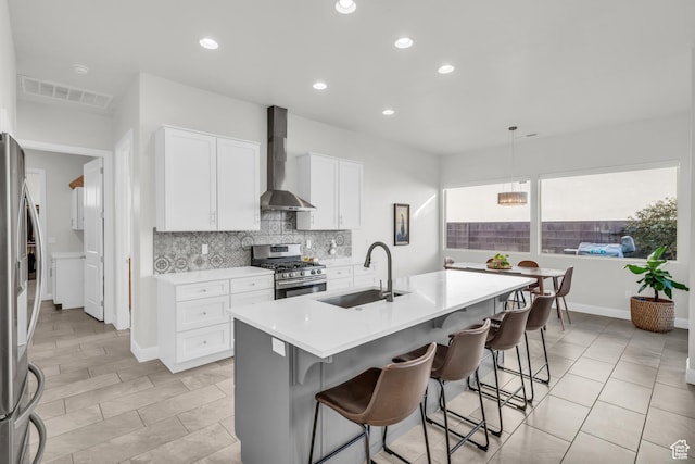 kitchen with a center island with sink, a breakfast bar area, appliances with stainless steel finishes, wall chimney exhaust hood, and sink