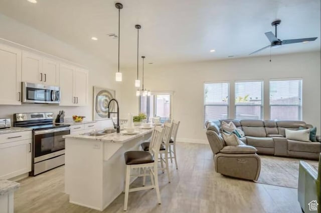 kitchen featuring appliances with stainless steel finishes, white cabinetry, sink, hanging light fixtures, and a kitchen island with sink