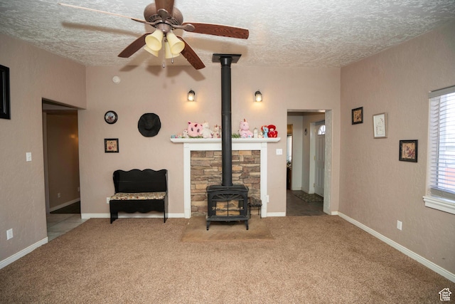 carpeted living room with ceiling fan, a textured ceiling, and a wood stove