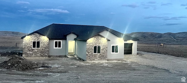 exterior space with stone siding, stucco siding, a mountain view, and a shingled roof