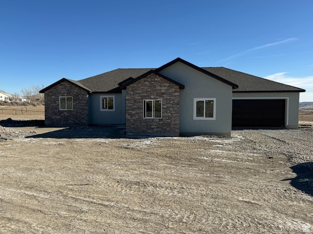 view of front of property with stone siding, driveway, an attached garage, roof with shingles, and stucco siding