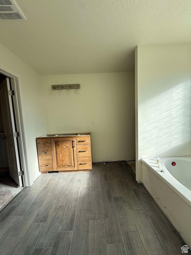 full bathroom featuring a textured ceiling, visible vents, wood finished floors, and a garden tub