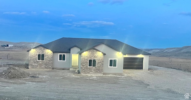 view of front of property with stone siding, fence, an attached garage, stucco siding, and a mountain view