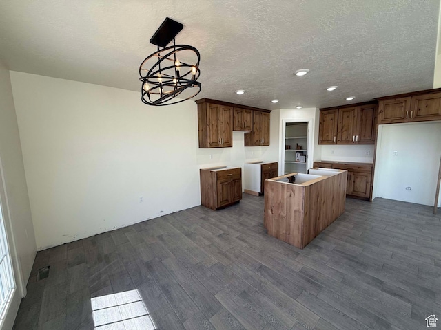 kitchen with dark wood-style flooring, a textured ceiling, visible vents, a chandelier, and a center island