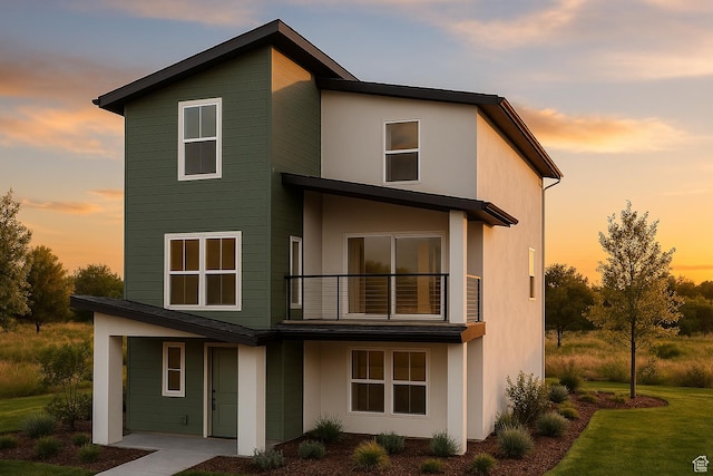 back of house with a balcony, stucco siding, and a yard
