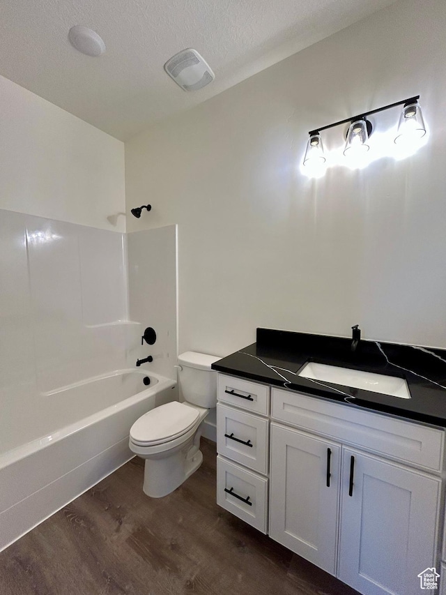 full bathroom featuring hardwood / wood-style floors, a textured ceiling, vanity, toilet, and bathtub / shower combination