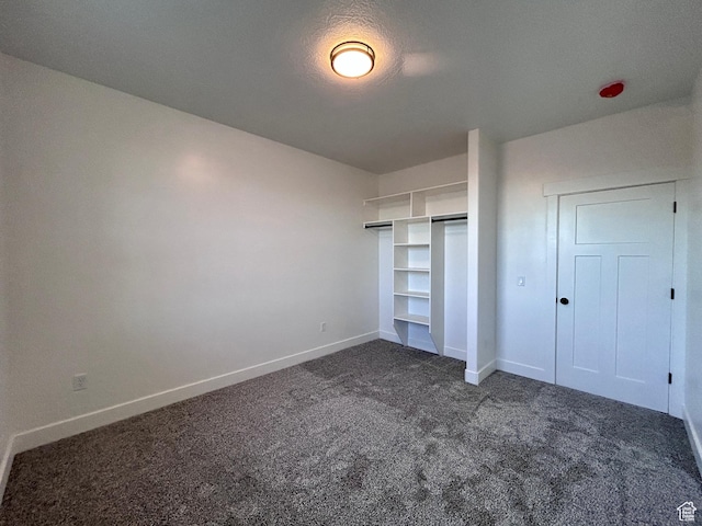 unfurnished bedroom with a textured ceiling, a closet, and dark colored carpet