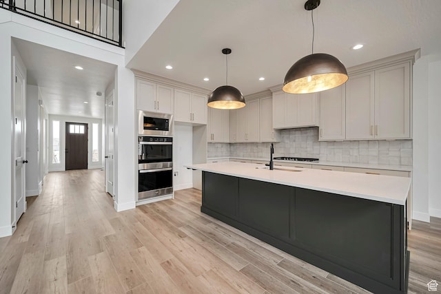 2946 N 1080 W, Lehi, UT 84043 - kitchen featuring appliances with stainless steel finishes, light wood-style floors, light countertops, a kitchen island with sink, and tasteful backsplash