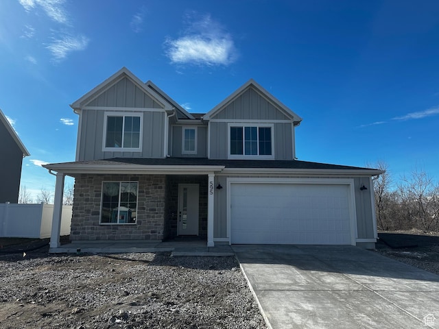 view of front of home with stone siding, fence, an attached garage, board and batten siding, and driveway