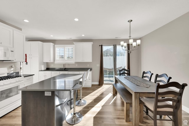 kitchen with decorative light fixtures, sink, white cabinetry, white appliances, and a center island