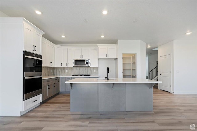 kitchen with double wall oven, gas stovetop, a sink, a center island with sink, and stainless steel microwave