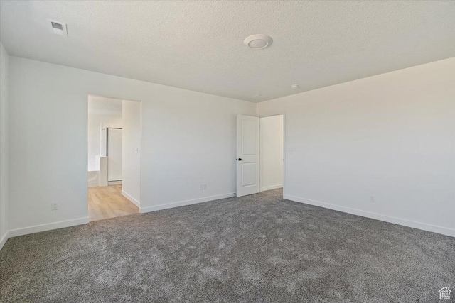 spare room featuring a textured ceiling, carpet floors, baseboards, and visible vents