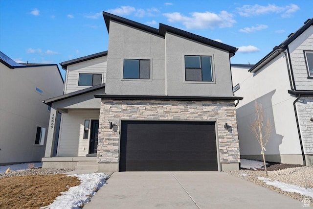 modern home with stone siding, stucco siding, an attached garage, and driveway