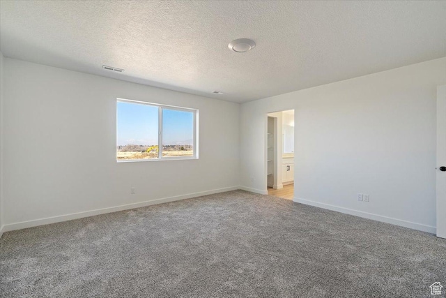 empty room featuring a textured ceiling, baseboards, visible vents, and light colored carpet
