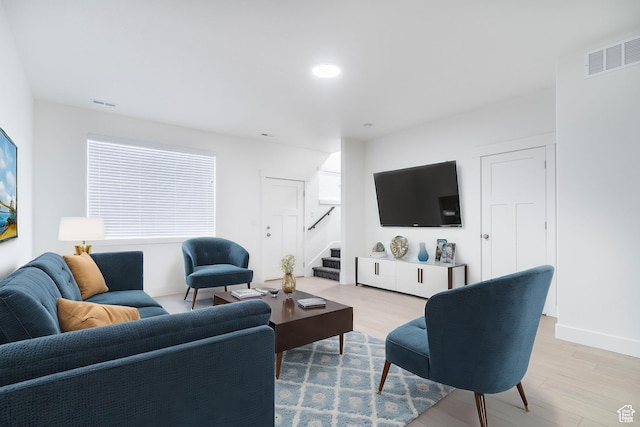 living room featuring baseboards, visible vents, light wood-style floors, and stairs