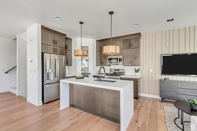 kitchen featuring hanging light fixtures, sink, light wood-type flooring, an island with sink, and stainless steel appliances