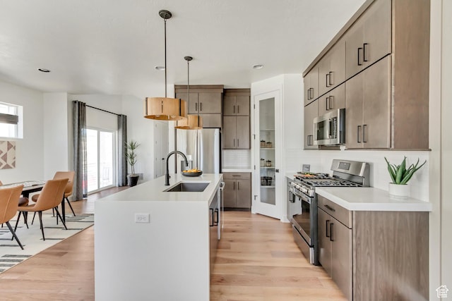 kitchen featuring sink, light wood-type flooring, pendant lighting, and stainless steel appliances