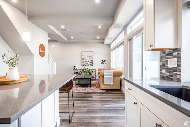 kitchen with wood finished floors, white cabinets, hanging light fixtures, decorative backsplash, and dark stone counters