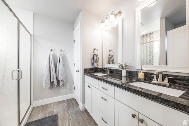 bathroom with double vanity, a stall shower, a sink, and baseboards