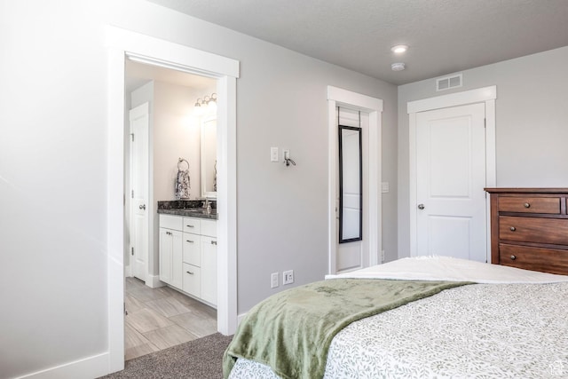 bedroom with ensuite bathroom, light colored carpet, a sink, visible vents, and baseboards